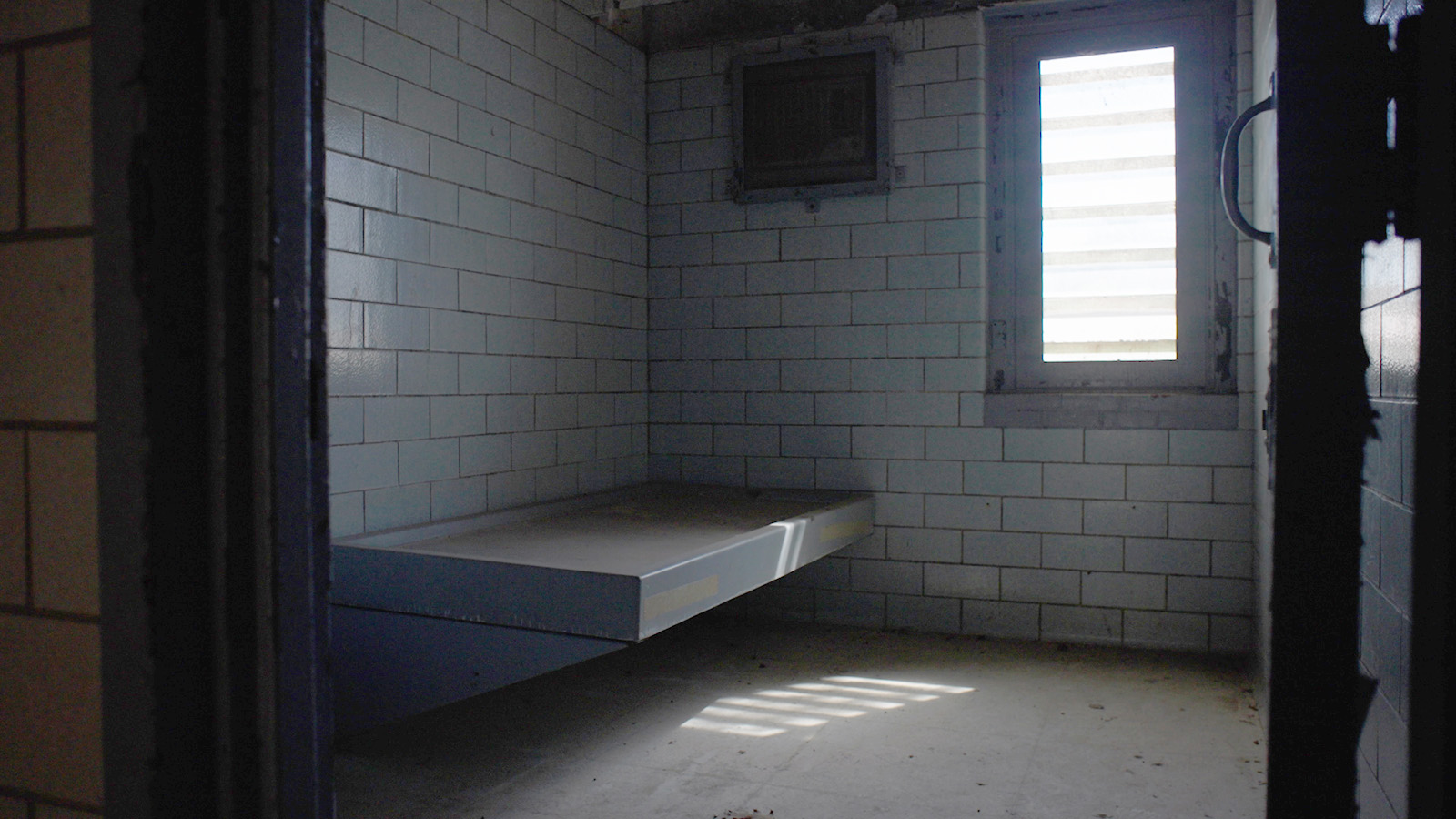 view of dark prison cell including bed platform and small window