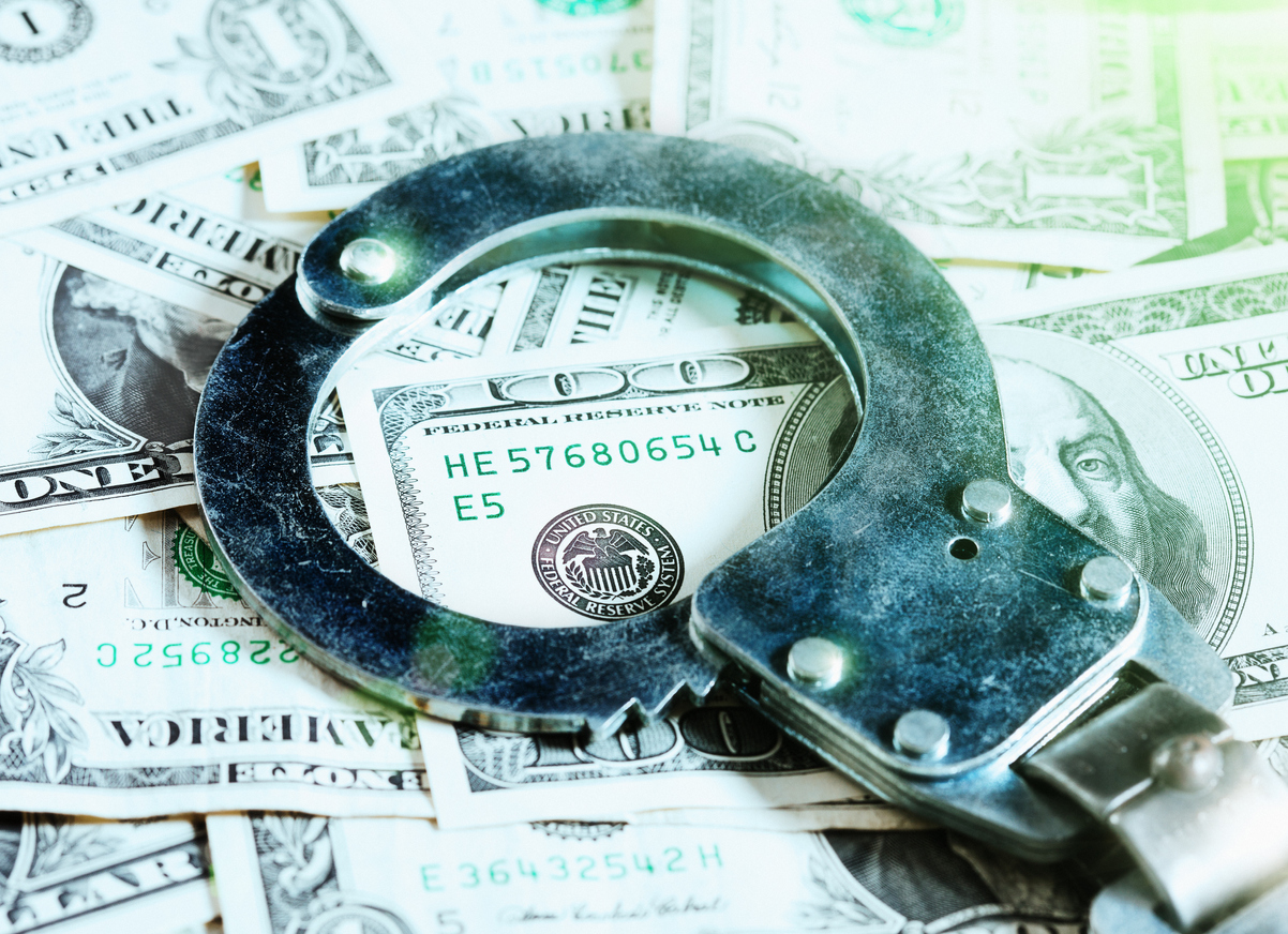 A pair of handcuffs rests on a US $100 bill among an abundance of dollars.