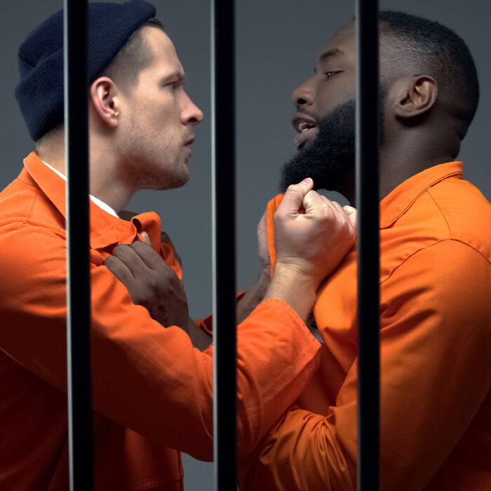 Black and white man behind bars, with their fists at each other's necks