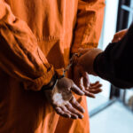 Man in an orange prison jumpsuit, with his hands cuffed behind his back