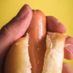 A hand holding a hot dog in a bun, symbolizing a man's penis