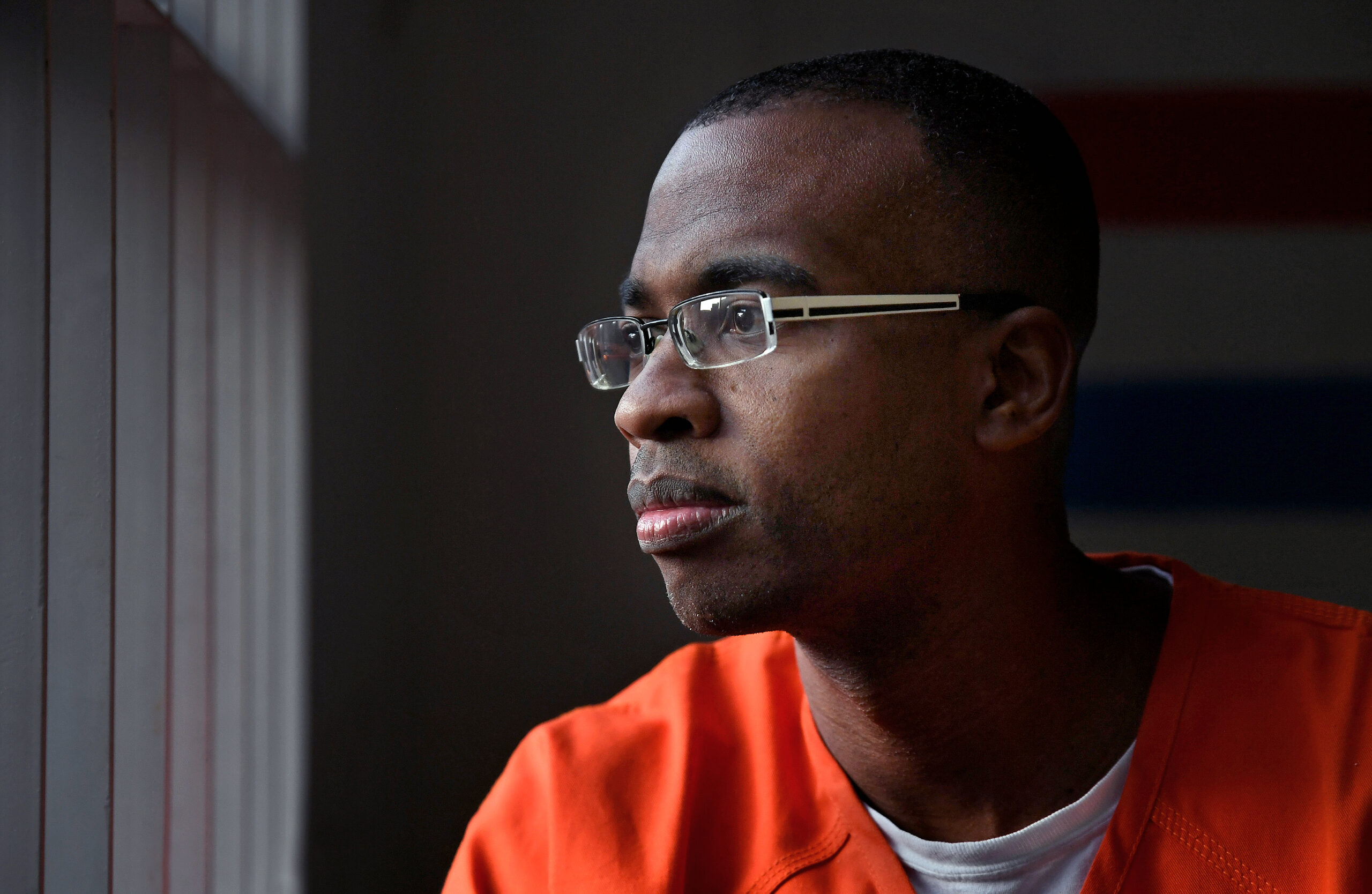 Joel Caston portrait: Man in prison jumpsuit with glasses