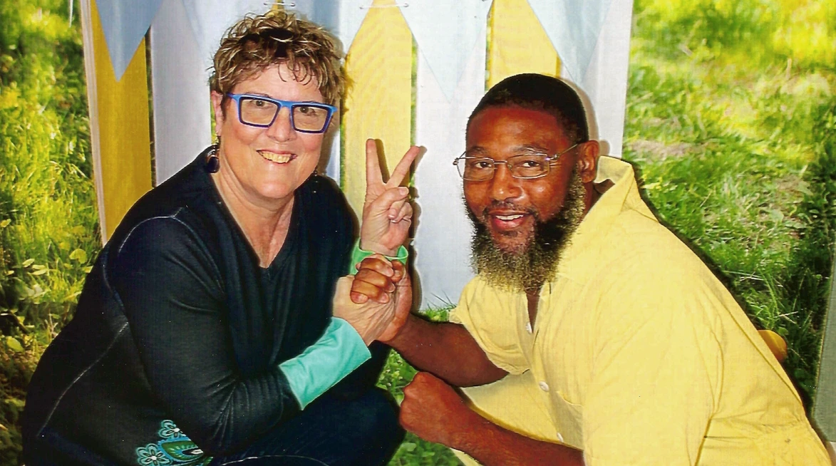 Pam Bailey and Rob Barton clasping hands and smiling. Pam has two fingers up as a peace sign.