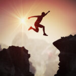 Silhouette of young man jumping over mountains and cliffs.